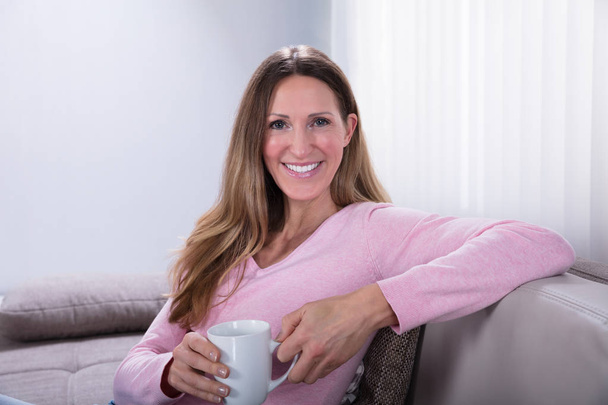 Happy Woman Sitting On Sofa Holding Coffee Cup At Home - Φωτογραφία, εικόνα