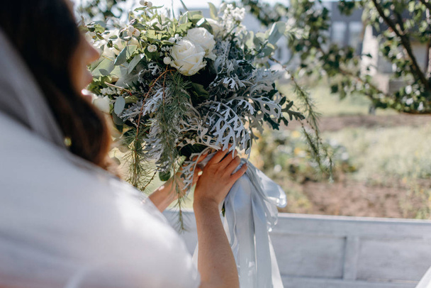 Closeup of bride binding ribbons on wedding bouquet in garden - Fotó, kép