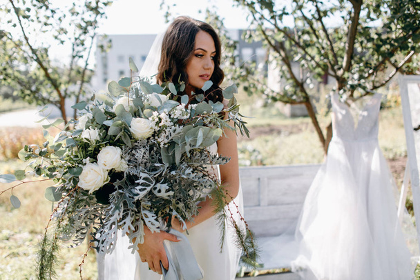 Portrait of pensive bride with wedding bouquet posing in garden - Φωτογραφία, εικόνα