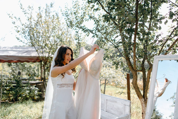 Side view of bride hanging wedding dress on branch in garden - Valokuva, kuva