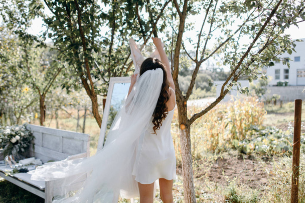 Bride hanging wedding dress on branch in garden - Foto, afbeelding