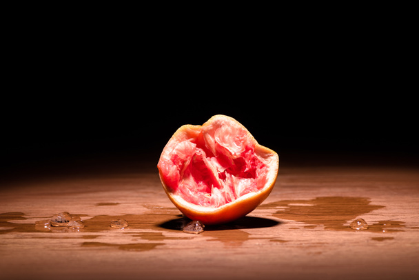 squeezed grapefruit on wooden table in dark room - Φωτογραφία, εικόνα