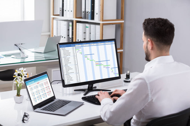 Businessman Analyzing Gantt Chart On Computer With Laptop Over Desk - 写真・画像