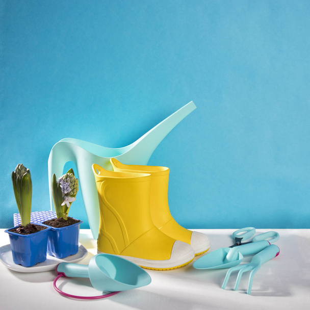 the Yellow rubber boots on the white wooden table on the blue background. Garden accessories. - Фото, изображение