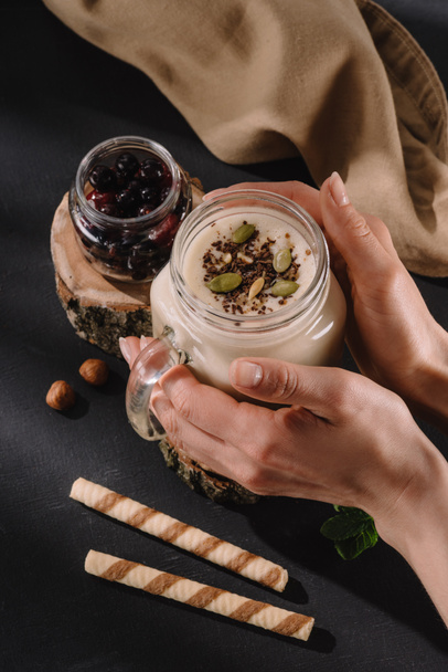 cropped image of female holding milkshake with chocolate shaving and pistachio nuts, sweet straws, currants, walnuts and mint  - Fotó, kép