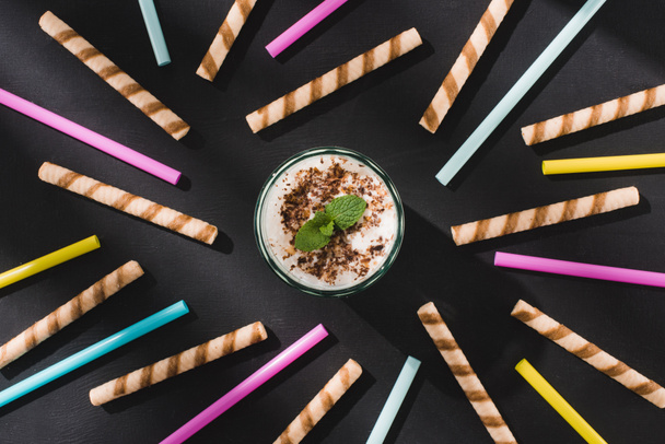 top view of milkshake with chocolate shavings and mint surrounded by sweet and drinking straws  - Zdjęcie, obraz