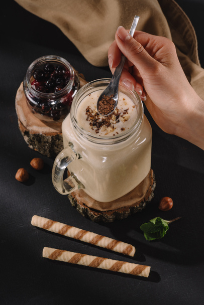 обрізаний знімок жіночої руки, що кладе шоколадну стружку в молочний коктейль, м'ята, солодкі соломинки і смородину на стіл
  - Фото, зображення