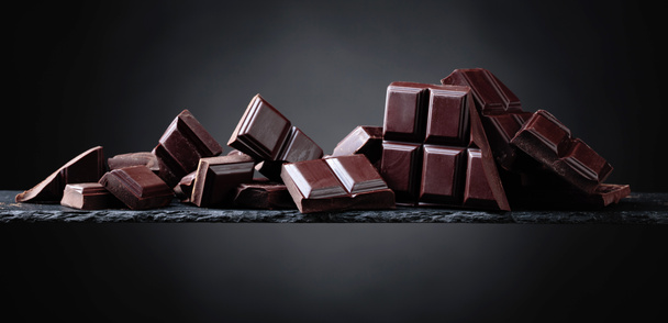 Pedaços de chocolate quebrados em um fundo preto
. - Foto, Imagem