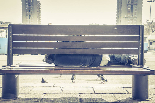 Poor homeless man or refugee sleeping on the wooden bench on the urban street in the city, social documentary concept - Fotoğraf, Görsel