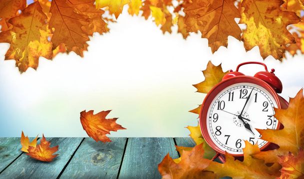 Clock and autumn leaves on wooden table - daylight saving time c - Photo, Image