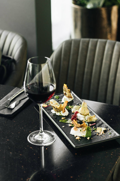 Weinglas mit Rotwein und Antipasti auf dem Tisch im Café  - Foto, Bild