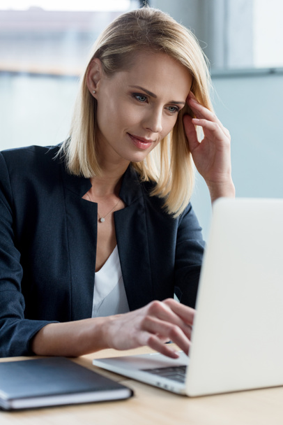 усміхнена блондинка бізнес-леді використовує ноутбук на робочому місці
 - Фото, зображення