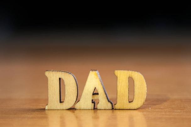 das Wort "Papa" aus Holzbuchstaben. Holzbeschriftung auf Tisch und dunkelschwarzem Hintergrund - Foto, Bild