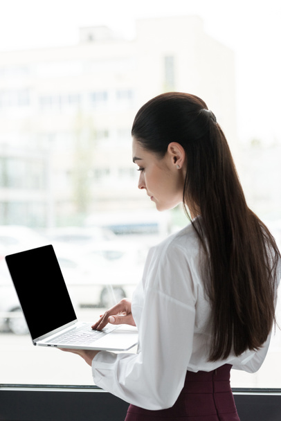 vue latérale de la jeune femme d'affaires à l'aide d'un ordinateur portable avec écran blanc
  - Photo, image