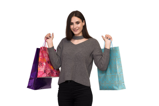 A beautiful brunette girl is standing on a white background and holding packages from a store and smiling. - Foto, afbeelding