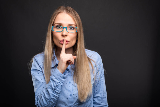 Geschäftsfrau mit blauer Brille zeigt Schweigegegeste - Foto, Bild