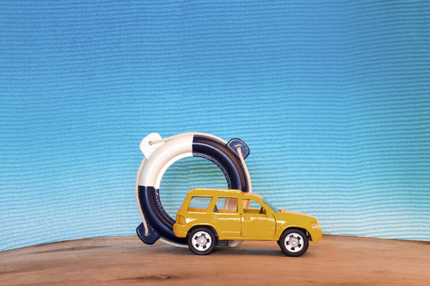 kleine gele auto en reddingsboei op blauwe achtergrond - Foto, afbeelding