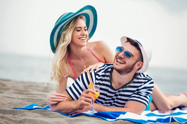 Feliz joven pareja tumbada en una playa y bebiendo cóctel
 - Foto, imagen