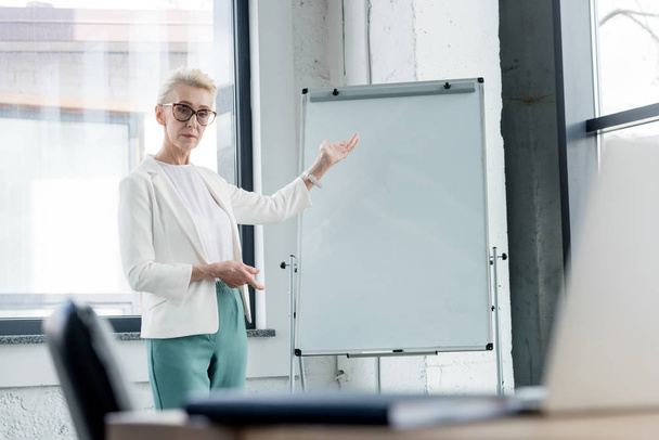 serious mature businesswoman in eyeglasses pointing at blank whiteboard - Photo, Image