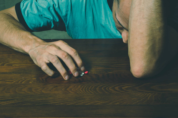 Depressed man suffering from suicidal depression want to commit suicide by taking strong medicament drugs and pills while he is sitting on the floor of his dark room - Foto, Bild