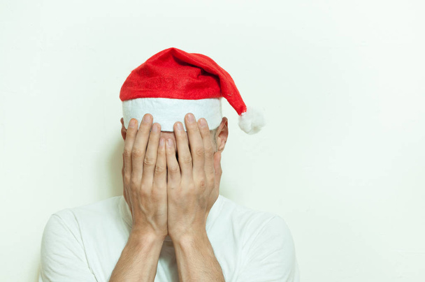Young man with Santa Claus hat cover his face with his hands feeling lonely and sad for New Year and Christmas holiday depression concept - Φωτογραφία, εικόνα