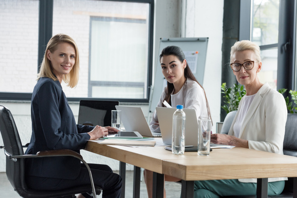 beautiful businesswomen sitting at meeting with gadgets in office - Φωτογραφία, εικόνα
