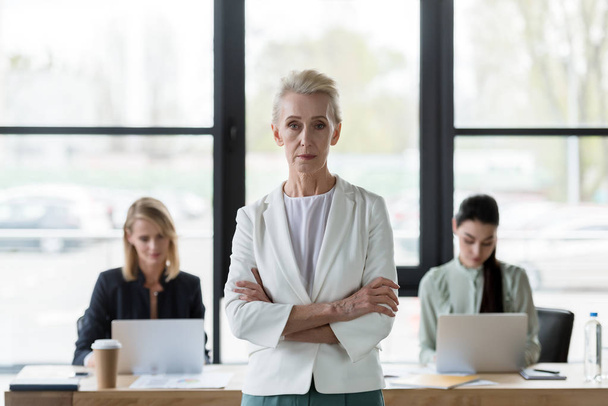 senior beautiful businesswoman standing with crossed arms and looking at camera in office - Foto, Imagen