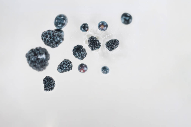 Juicy berries dropping into milk on white background - Photo, Image