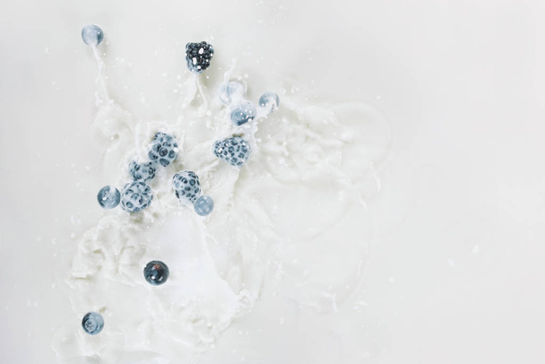 Splashes of milk with raw berries on white background - Foto, afbeelding