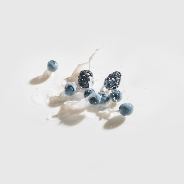 Berries dropping in milk with splashes on white background - Foto, afbeelding