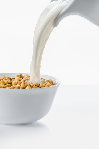 Maito kaatamalla kannu kulhoon soija valkoisella pohjalla
 - Valokuva, kuva
