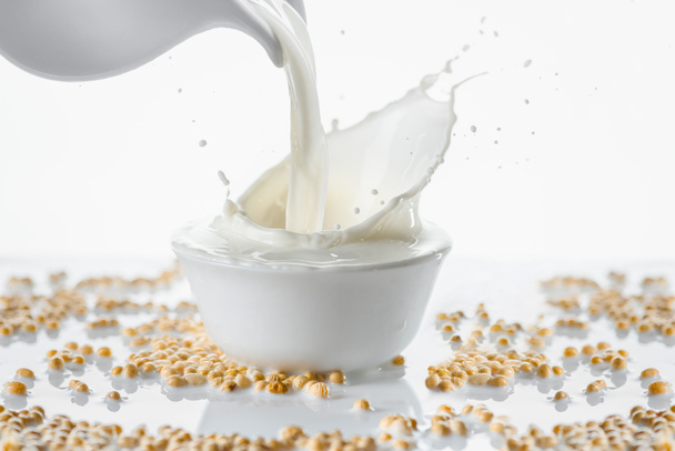 Milk splashing from jug in bowl with soybeans on white background - Φωτογραφία, εικόνα