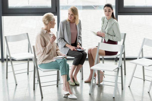 профессиональные предпринимательницы, сидящие на стульях и разговаривающие в офисе
 - Фото, изображение