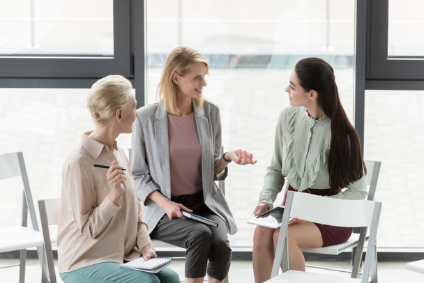 beautiful businesswomen sitting on chairs and talking in office - Photo, Image