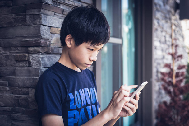 Asiático menino adolescente usando smartphone, luz do dia ao ar livre
. - Foto, Imagem