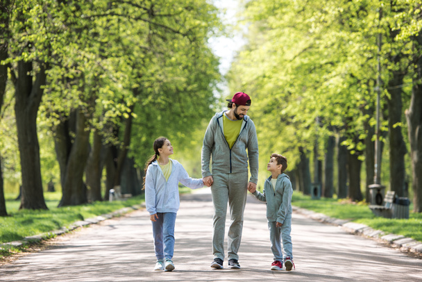 uśmiechnięty ojciec trzymając się za ręce, syn i Córka, i spacery w parku - Zdjęcie, obraz