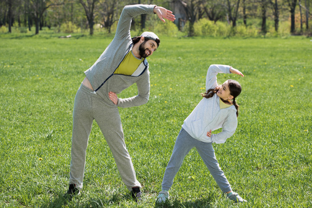 smiling daughter and father doing physical exercise on meadow in park - Foto, Imagen