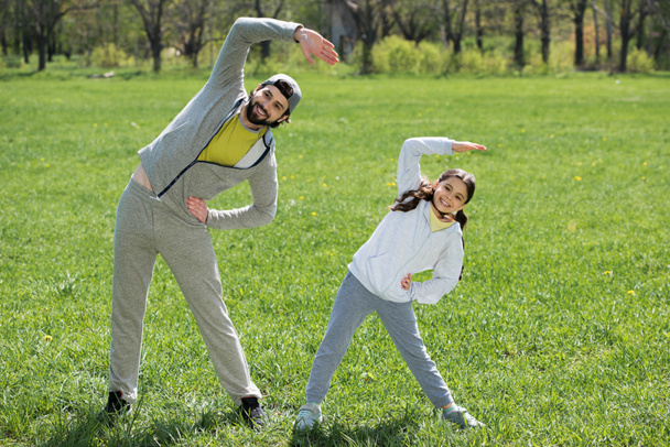 tytär ja isä tekevät liikuntaa ruoholla
 - Valokuva, kuva
