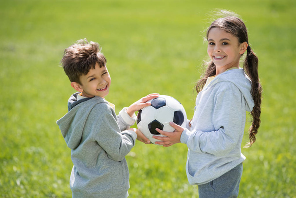 sonriente hermano y hermana sosteniendo pelota en el prado
  - Foto, Imagen