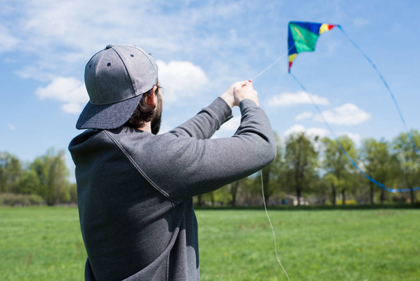 rear view of man flying kite on grassy meadow in park - Фото, изображение