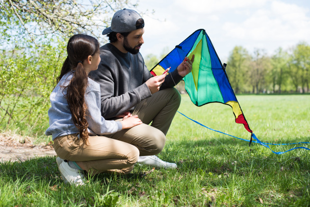 side view of father and daughter sitting with kite on meadow - Fotografie, Obrázek
