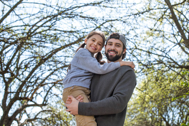 Tiefansicht eines lächelnden Vaters, der Tochter im Park hält - Foto, Bild