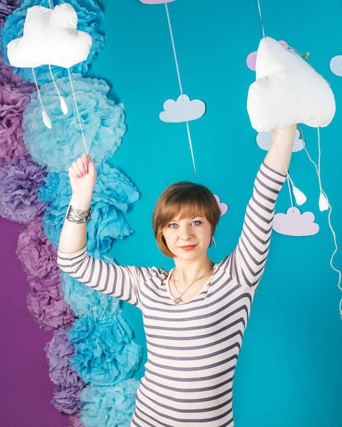 Beautiful lovely young caucasian girl holding clouds on blue background. - Fotó, kép