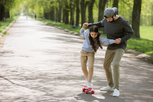 батько допомагає дочці кататися на скейтборді на шляху в парку
  - Фото, зображення