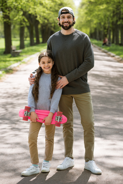 daughter with skateboard and father on path in park - Fotó, kép