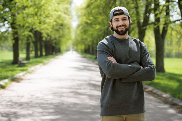 улыбающийся мужчина, стоящий со скрещенными руками на дорожке в парке
 - Фото, изображение