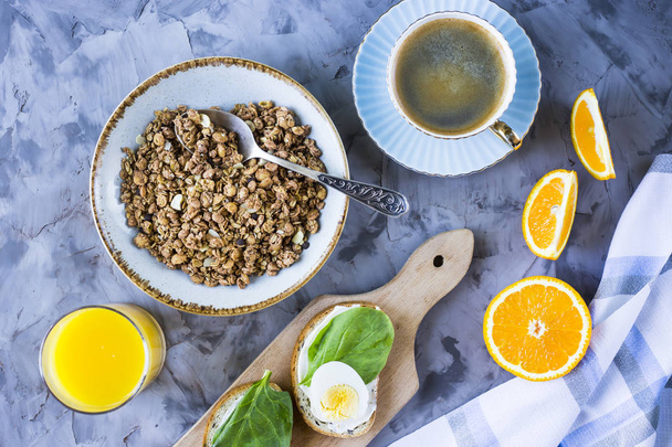 Gezonde stevig ontbijt - muesli, broodje met ei, koffie, sinaasappel en SAP op een grijze achtergrond. Bovenaanzicht - Foto, afbeelding