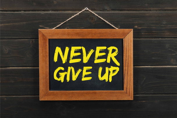 blackboard with inscription never give up hanging on wooden wall - Фото, изображение