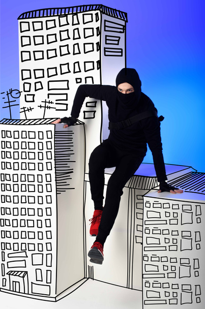 ninja in black clothing with katana behind getting across on drawing buildings on blue - Фото, зображення
