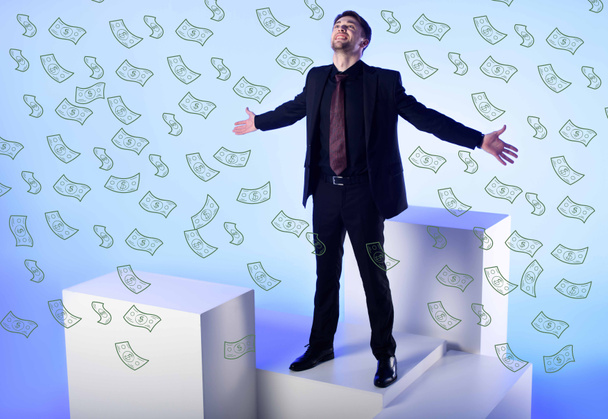 επιχειρηματία σε μαύρο κοστούμι με τα χέρια απλωμένα στέκεται στο λευκό μπλοκ με πτώση δολαρίου τραπεζογραμματίων στο μπλε - Φωτογραφία, εικόνα